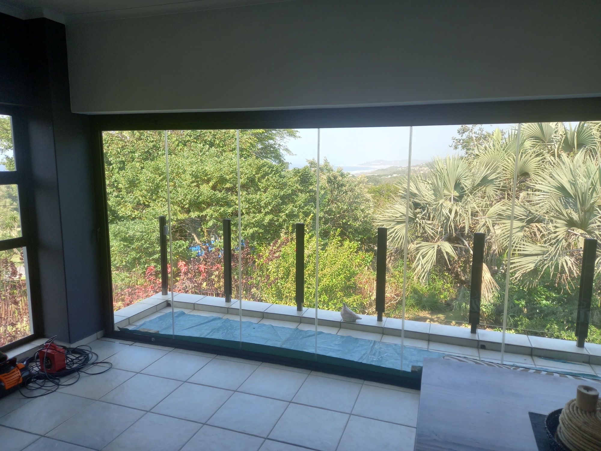 Stacking glass doors opening onto the balcony, with the sea beyond the treetops
